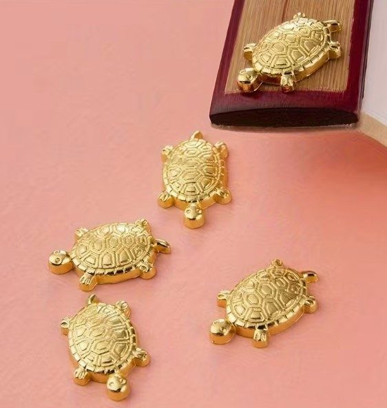 Japanese Money Turtle Four decorative golden turtle charms on a pink background.